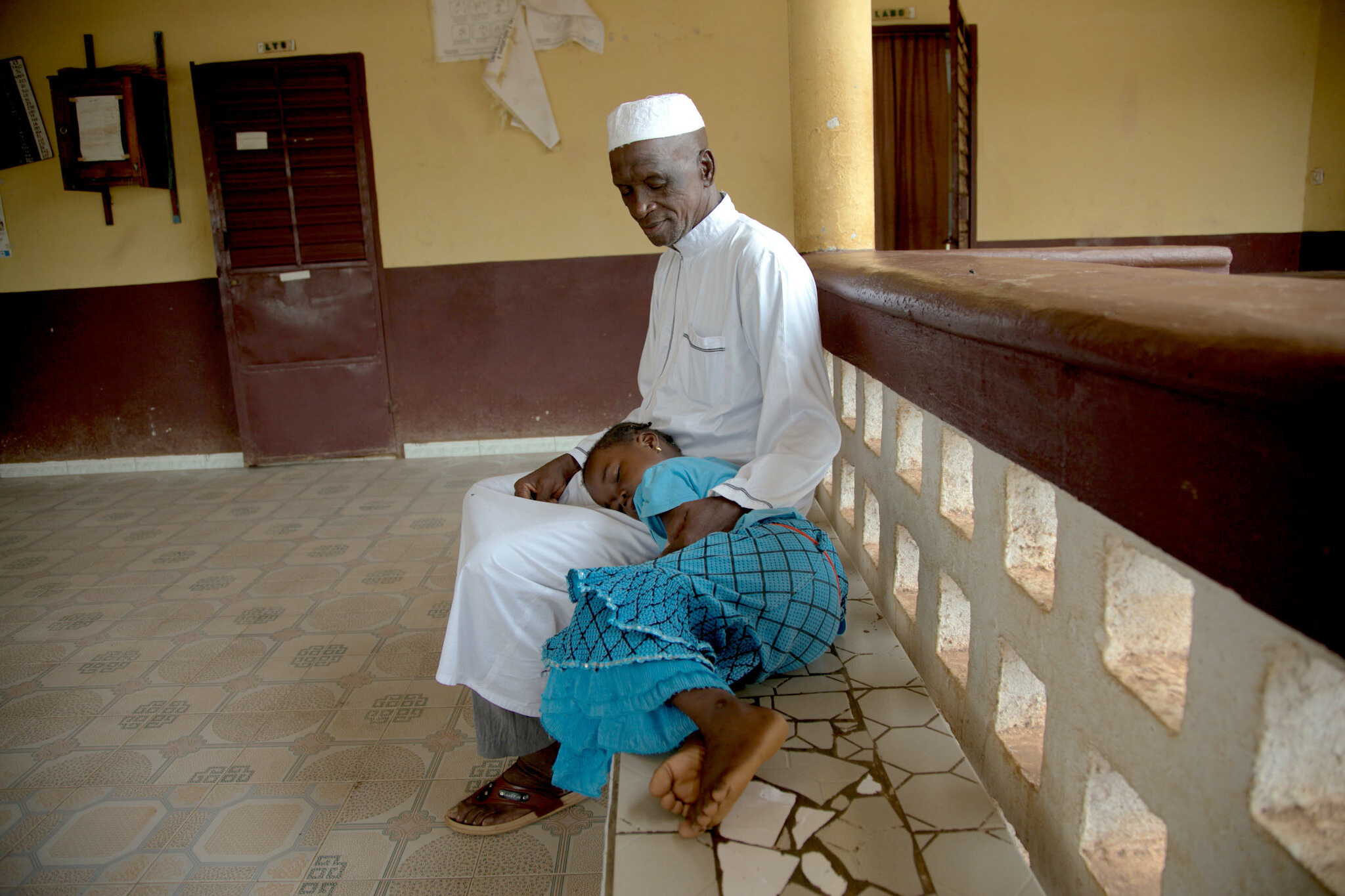 A-man-and-young-girl-wait-at-health-center-in-Faranah-Guinea-Patrick-Adams A man and his daughter at a health facility in Faranah, Guinea.