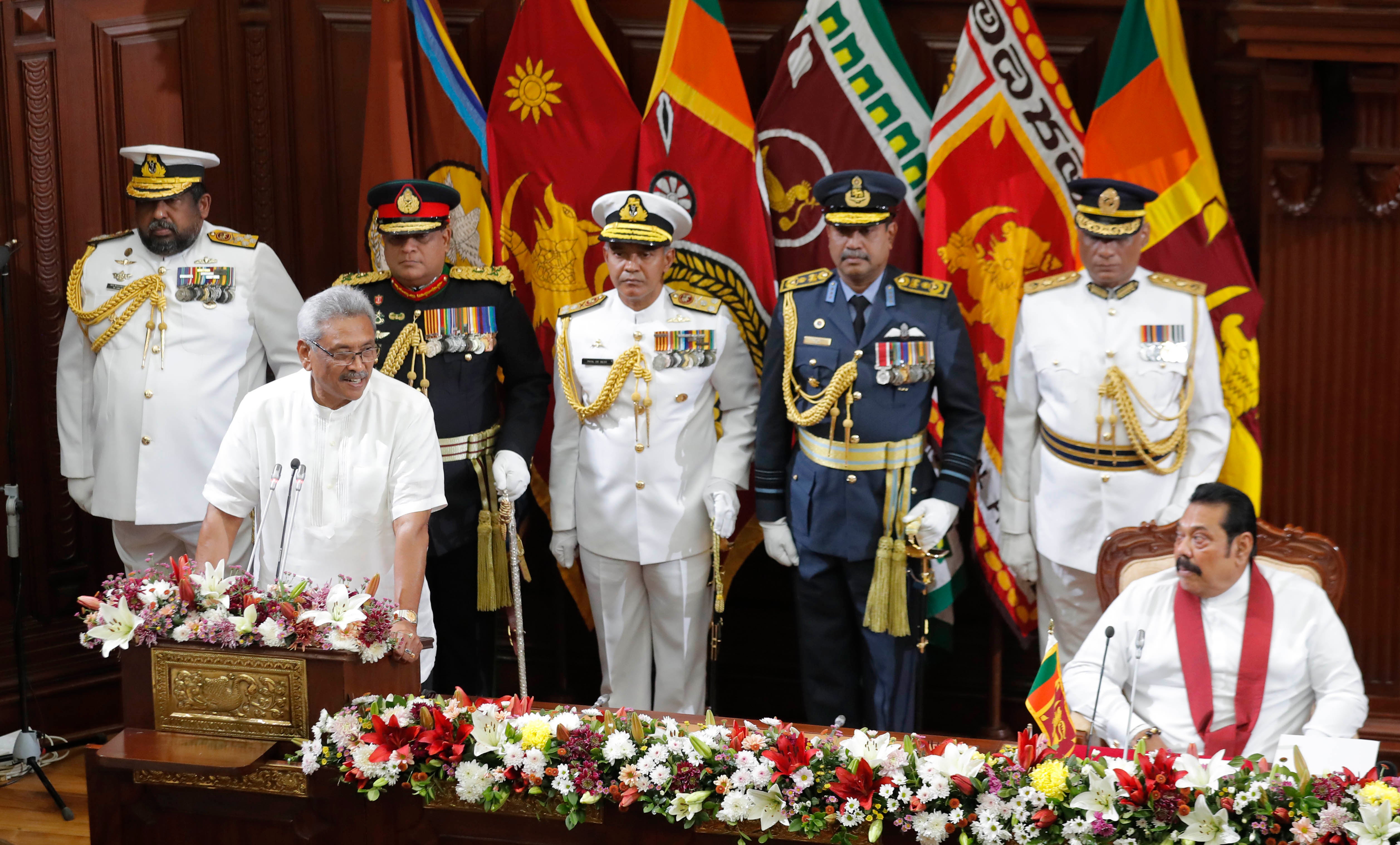 A man in white stands at a podium in front of uniformed military officers