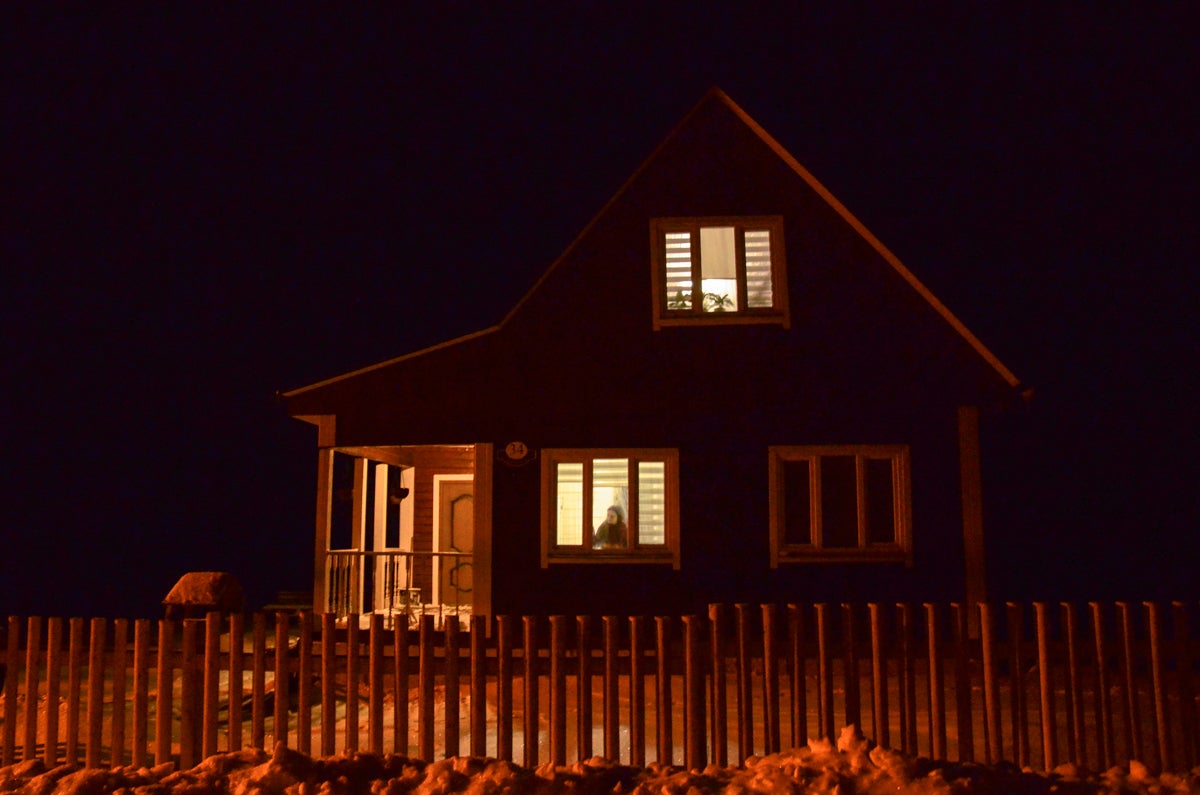 Yulia Alsheuskaya looking through the window of her house outside of Minsk, which she shares with her husband Siarhei who is currently in detention, January 2021.