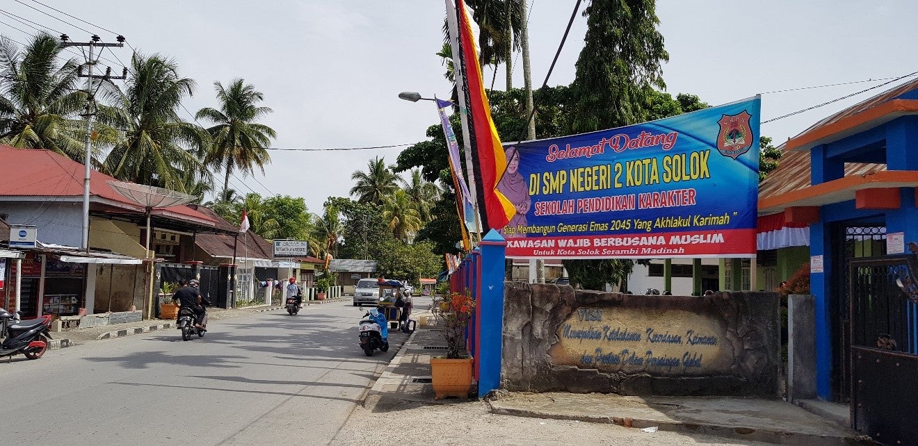 A billboard in front of a school, next to a paved road