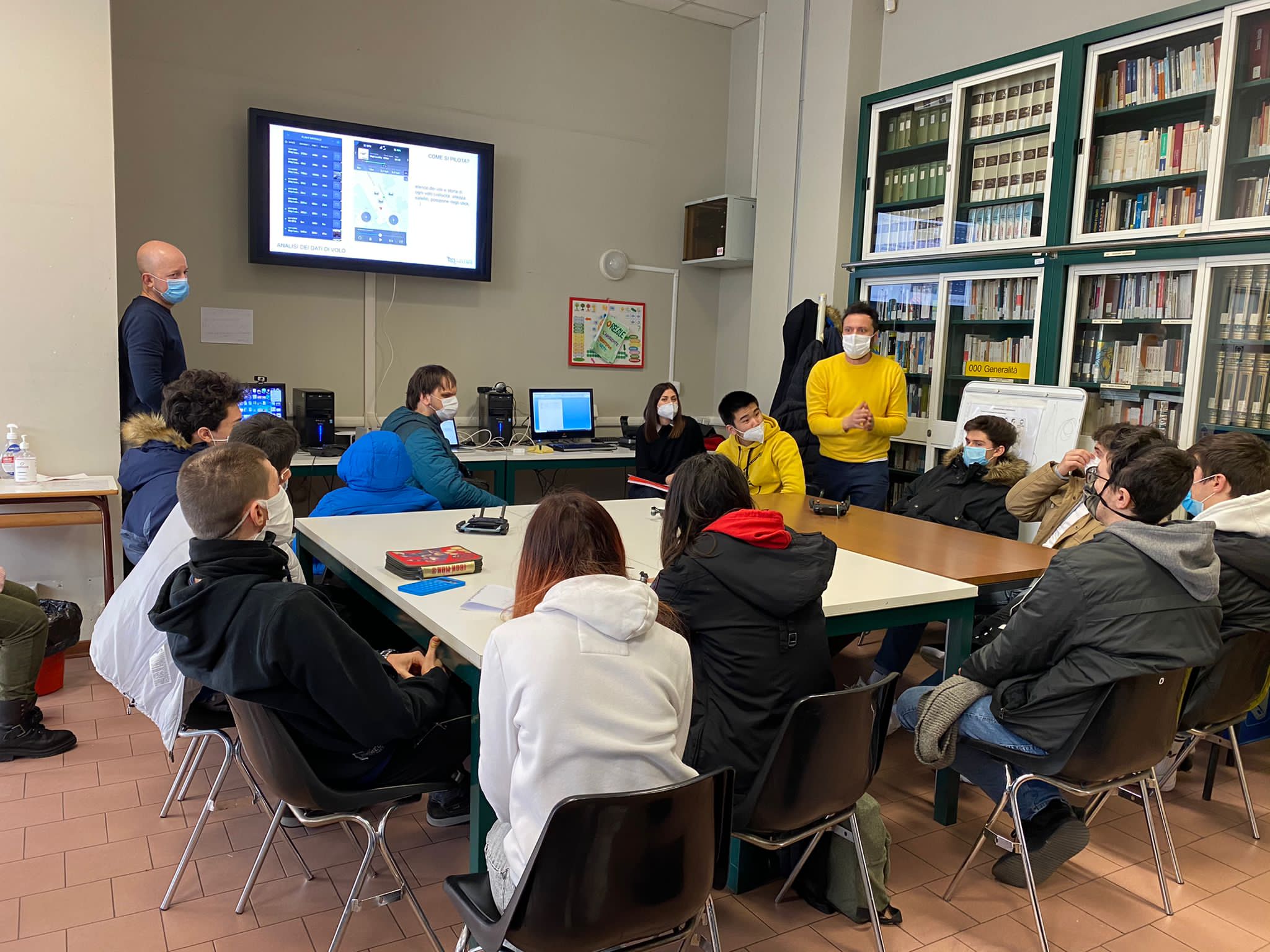 Studenti seduti intorno a una tavola, mentre ascoltano un insegnante.