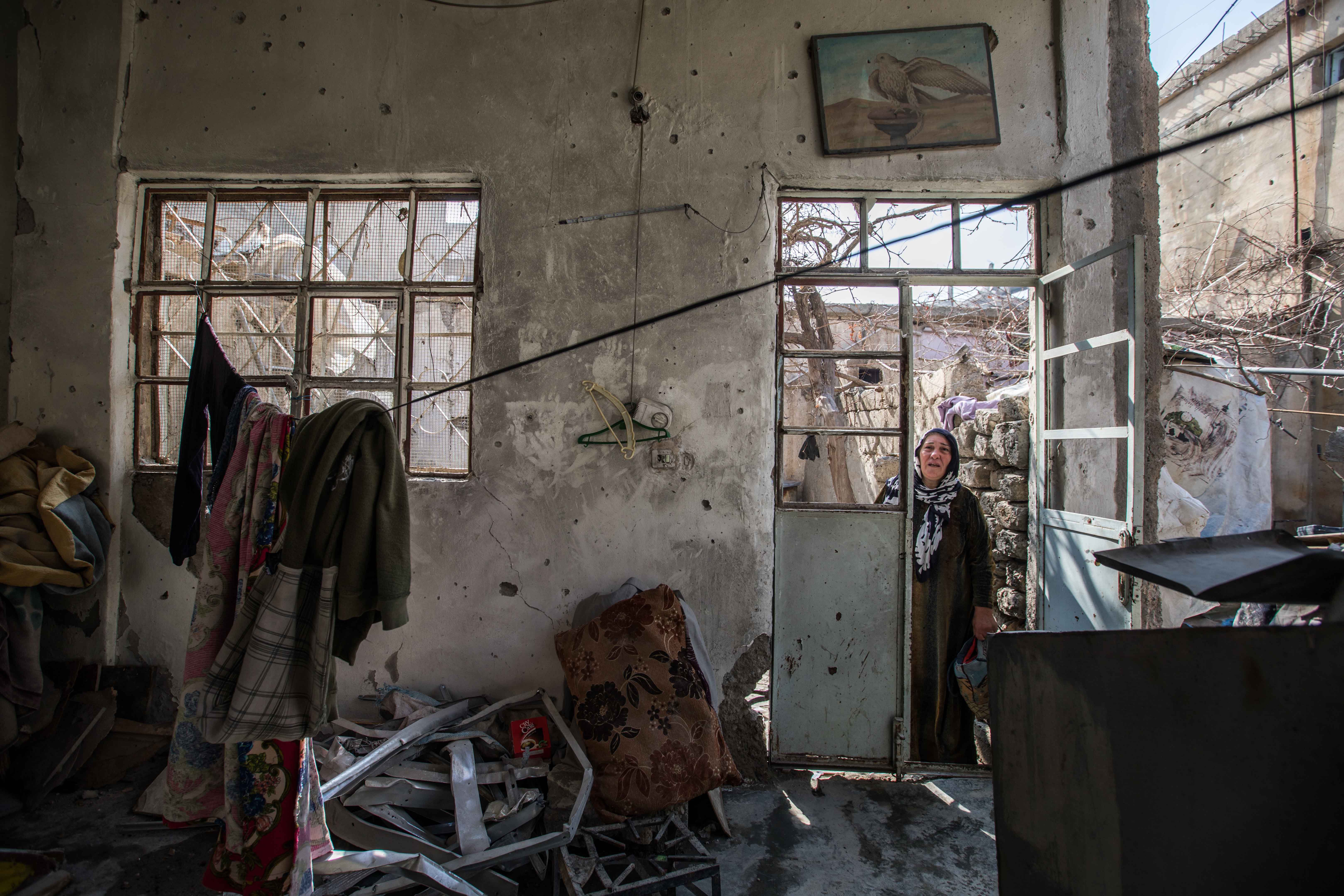 An older woman stands in the doorway of a destroyed home