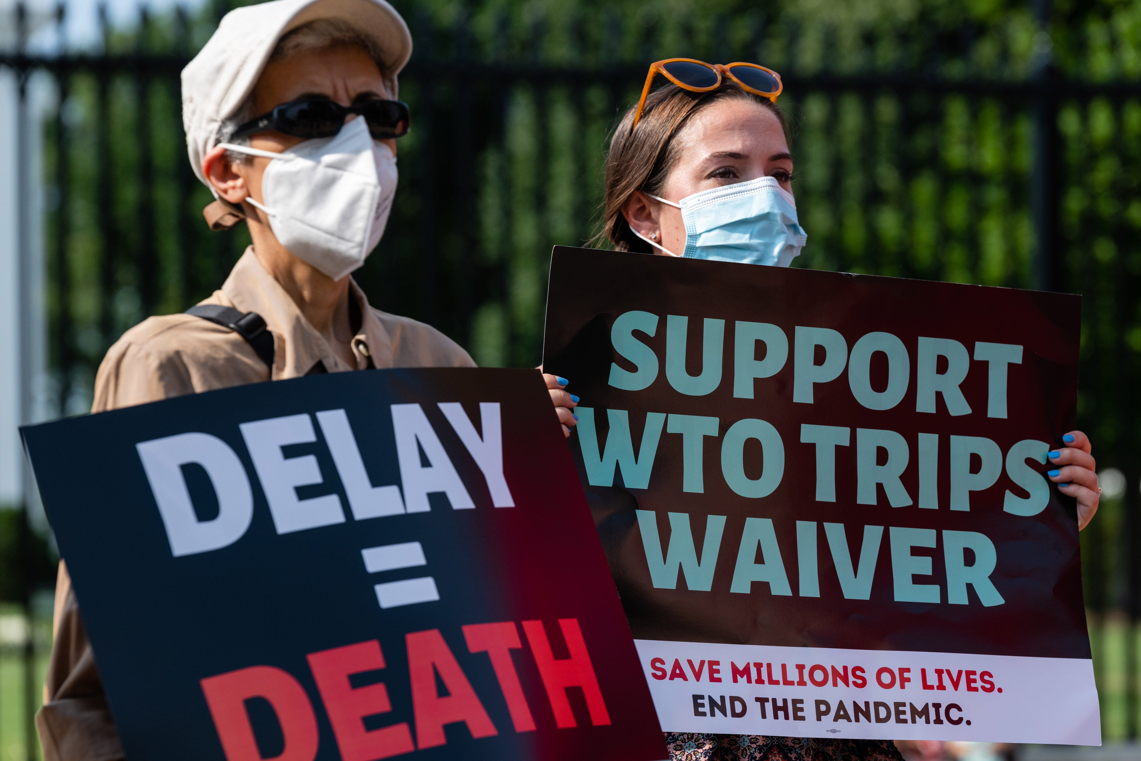 Protesters hold signs reading "Delay = Death" and "Support WTO Trips Waiver" during a demonstration ahead of the visit of German Chancellor Angela Merkel near the White House in Washington, DC, on July 15, 2021.