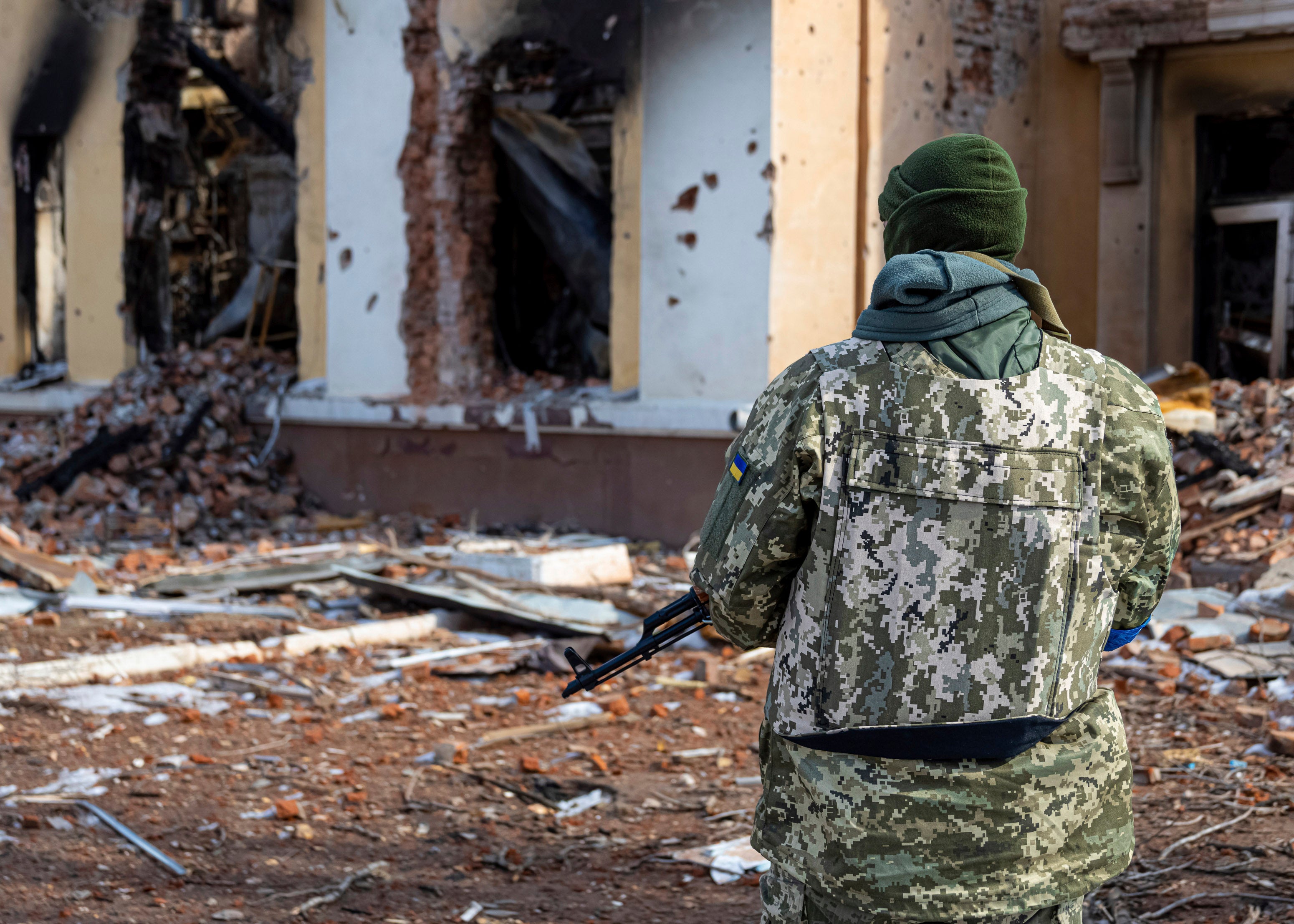 A soldier stands in front of a destroyed building