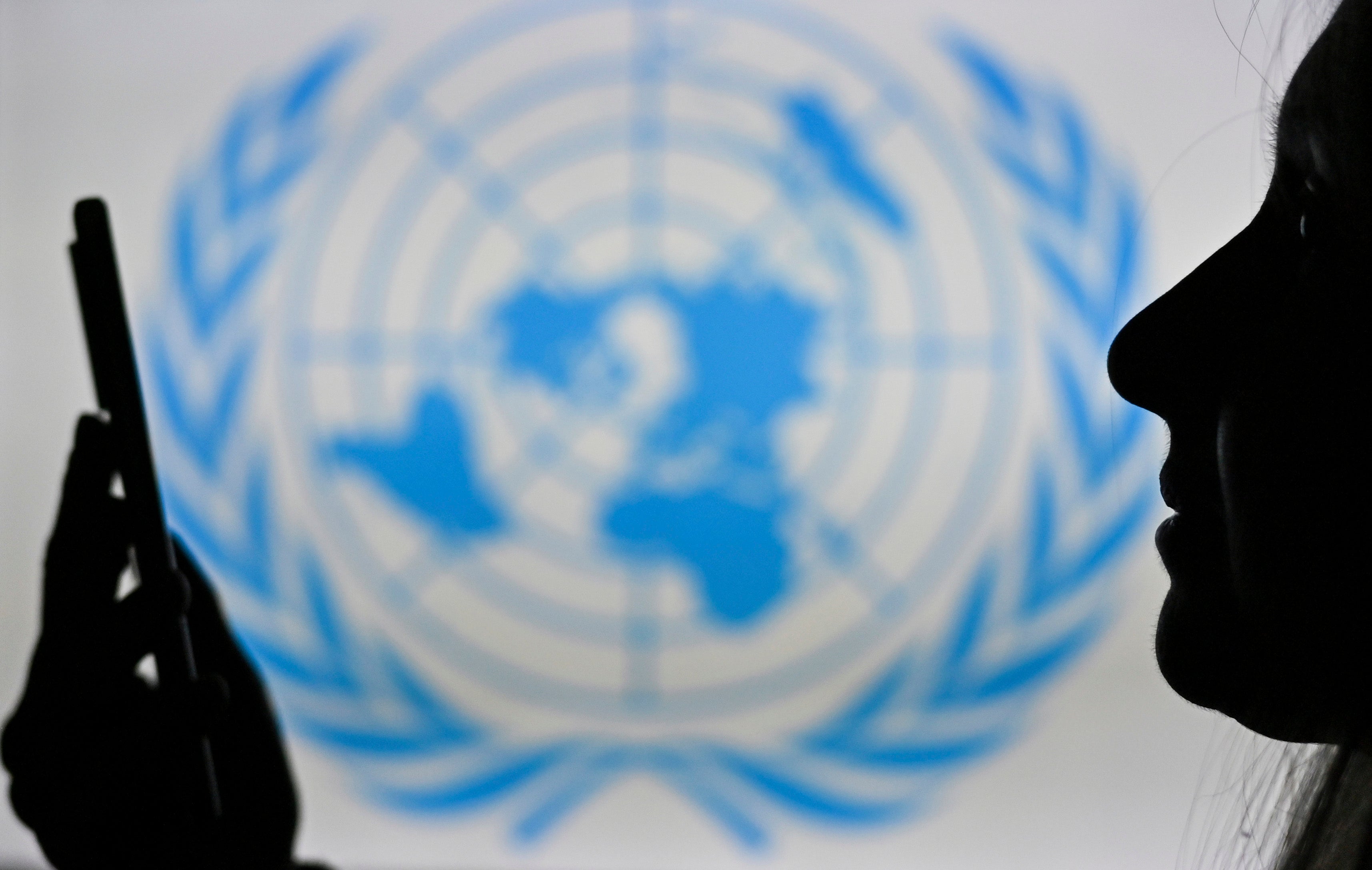 A woman looks at her cell phone in front of the United Nations logo displayed on a computer screen.