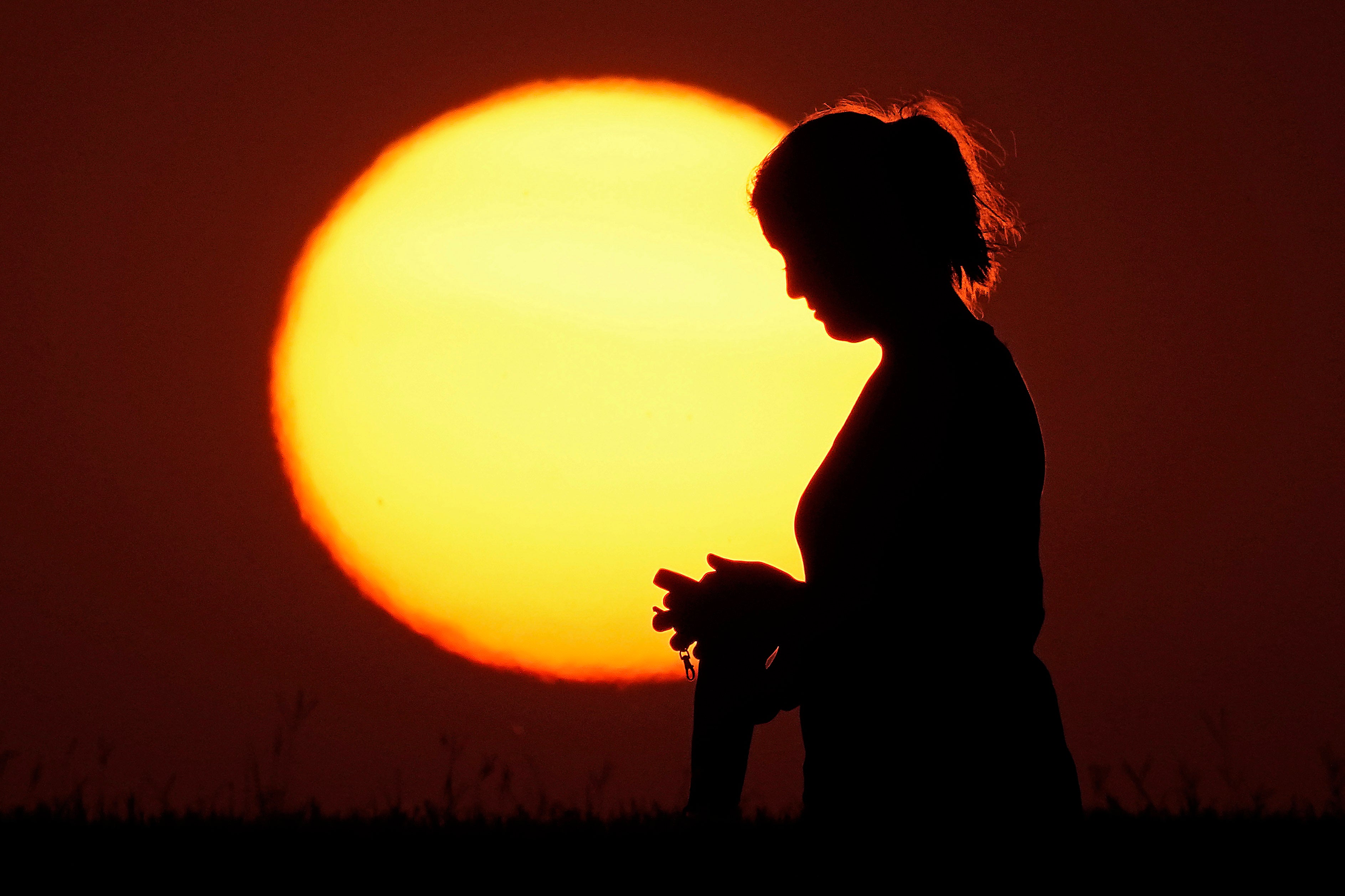 A woman stands in front of a setting sun