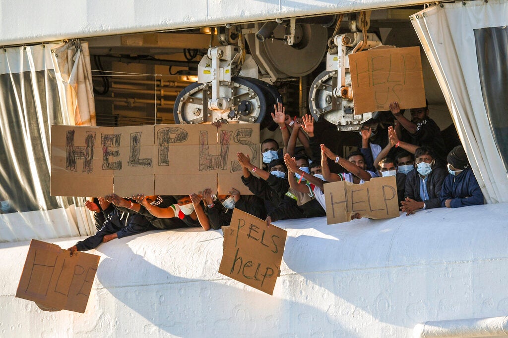 Migrants hold banners asking for help from a deck of the Geo Barents rescue ship operated by Doctors Without Borders, in Catania's port, Sicily, southern Italy, November 7, 2022