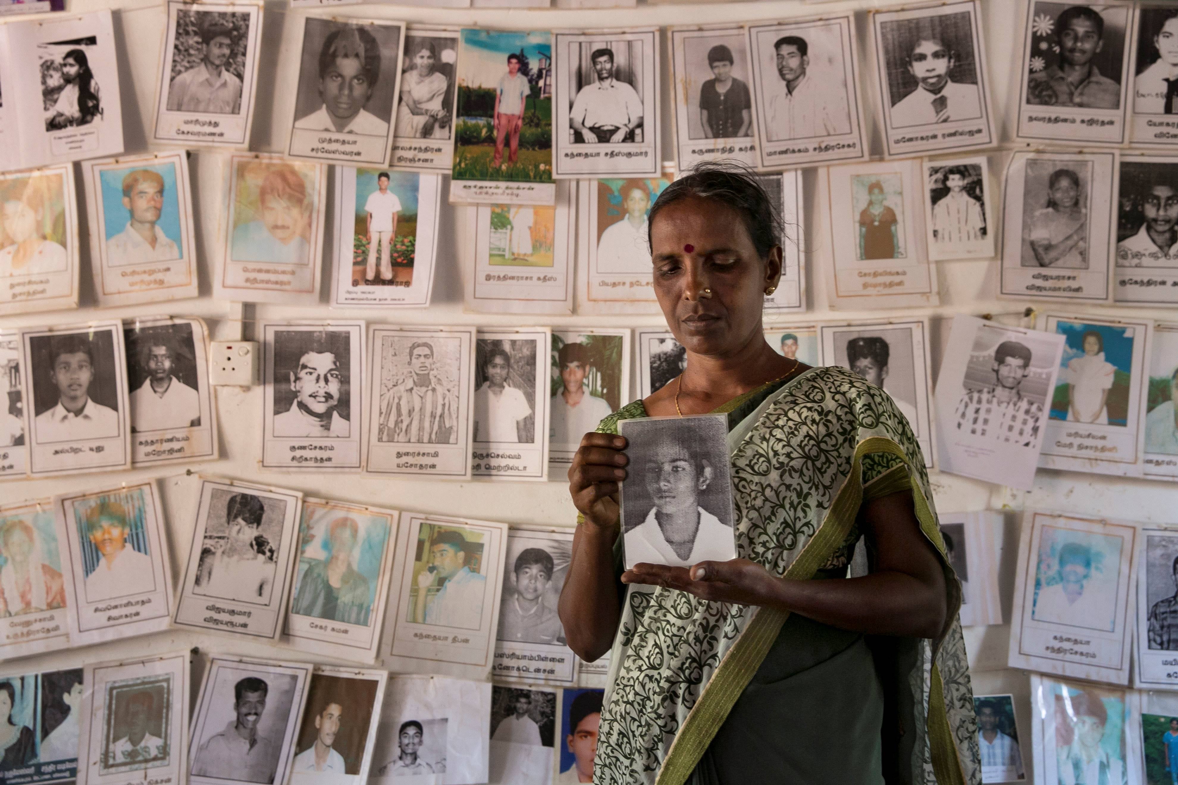 A woman holds a framed photo in front of a wall of other photos