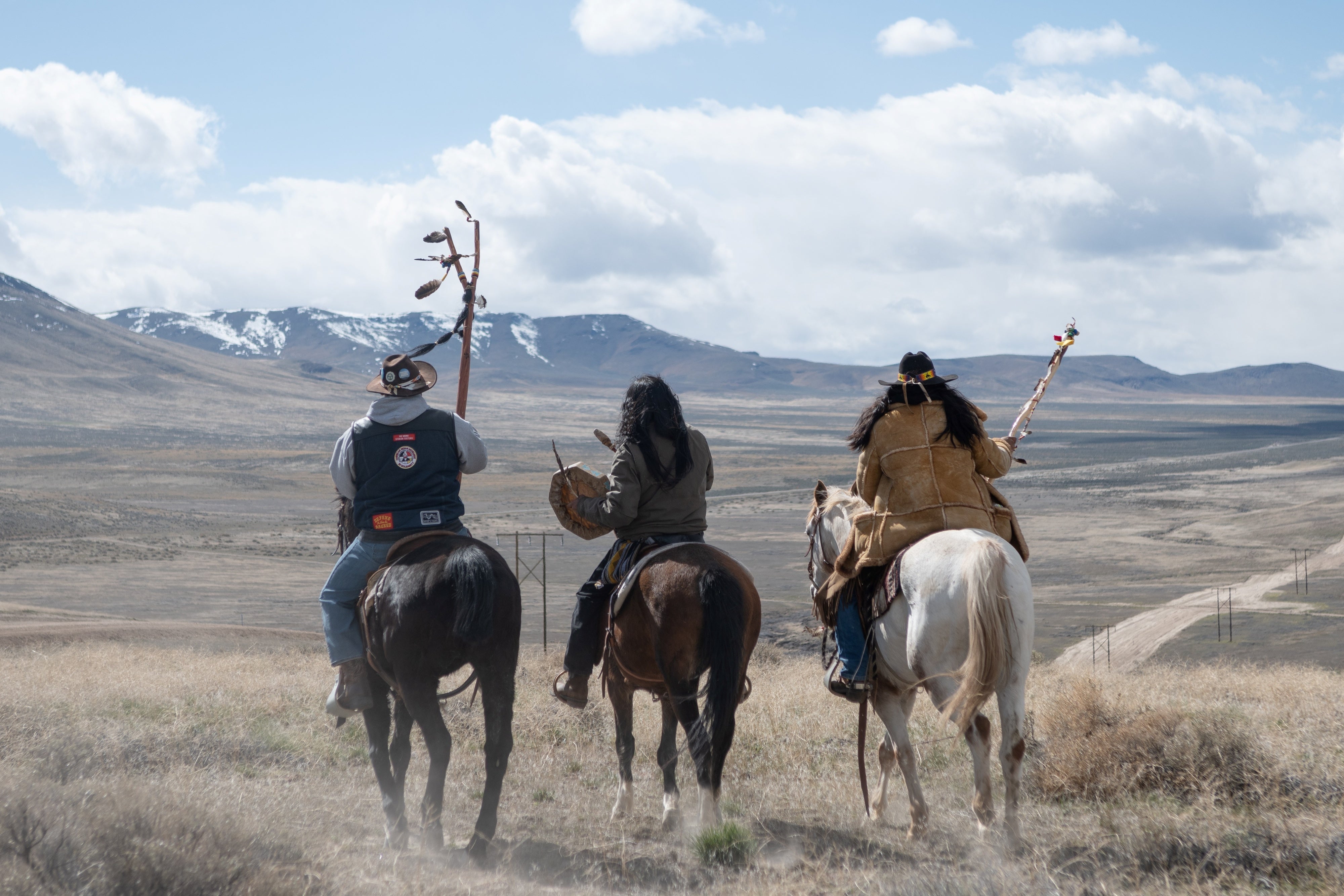 Three men sit atop horses overlooking a valley 