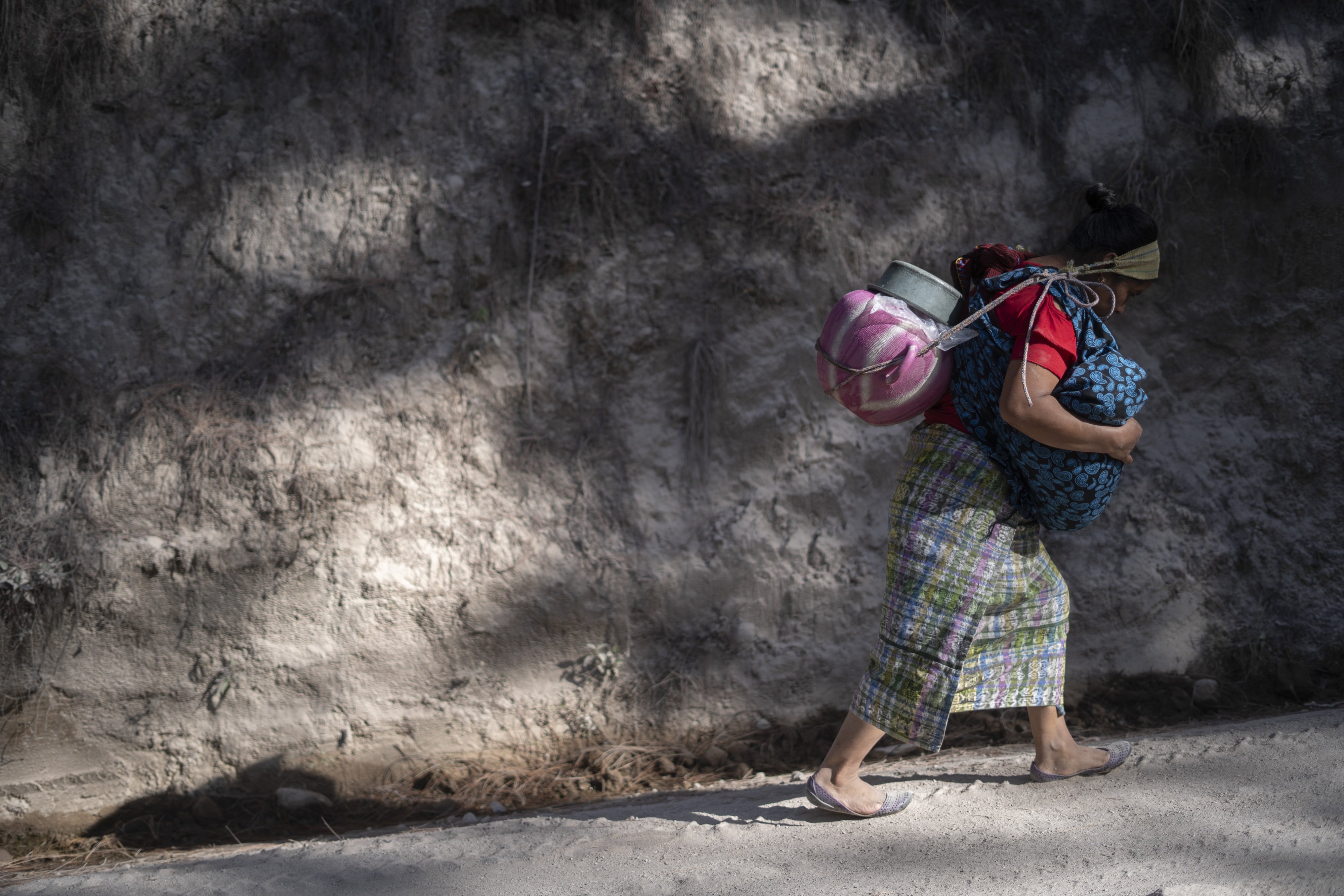 A woman transports water on her back while carrying her youngest son in her arms