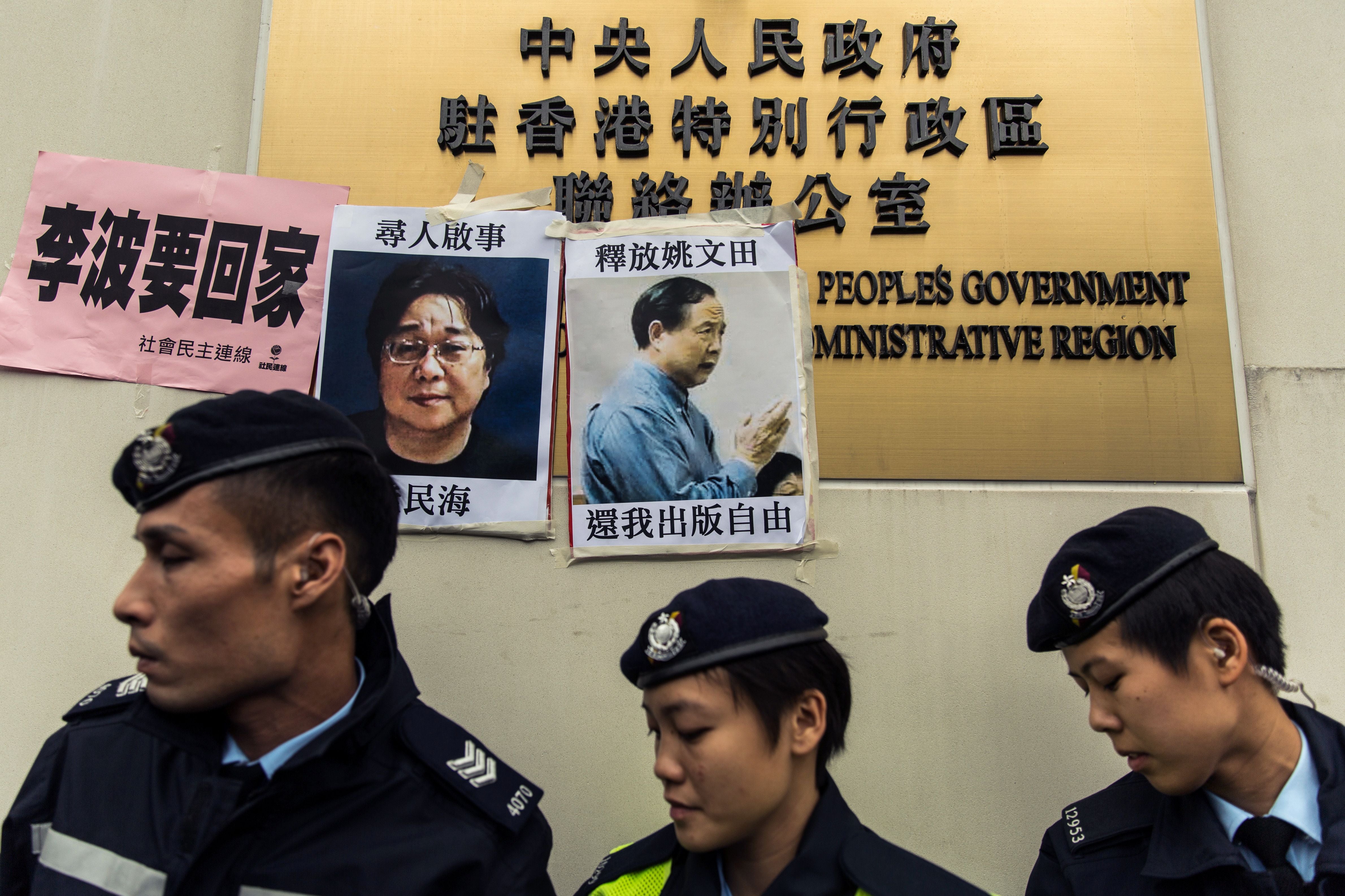 Police walk past missing person notices for Swedish publisher Gui Minhai (L) and Hong Kong publisher Yau Wentian, posted on the sign of China's Liaison Office in Hong Kong, January 3, 2016.