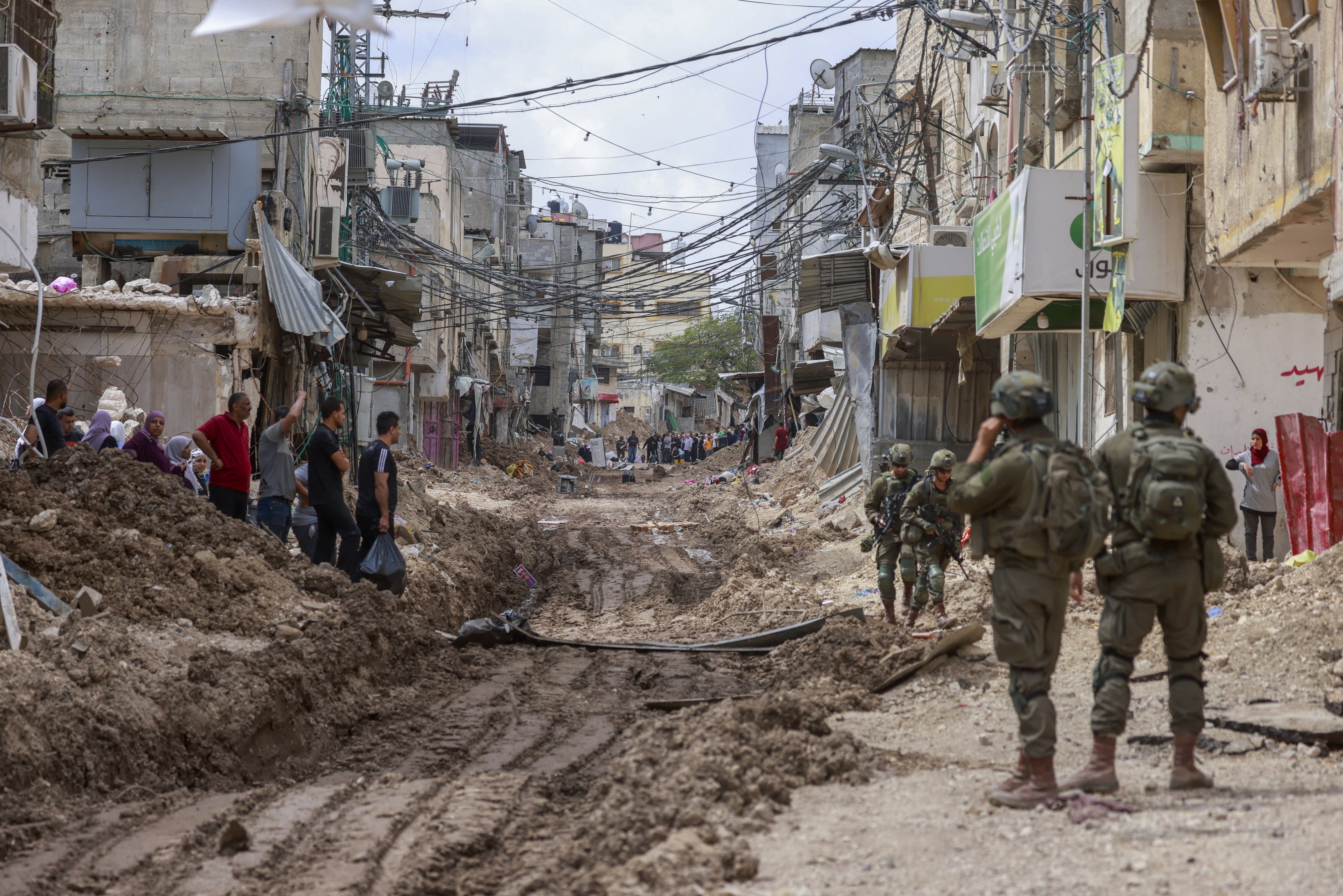 Israeli soldiers look on as Palestinian men and women carry their belongings on May 2, 2025 amid ongoing Israeli military operations and demolition of homes in Tulkarem refugee camp. Israeli forces had emptied the refugee camp of its inhabitants weeks prior.