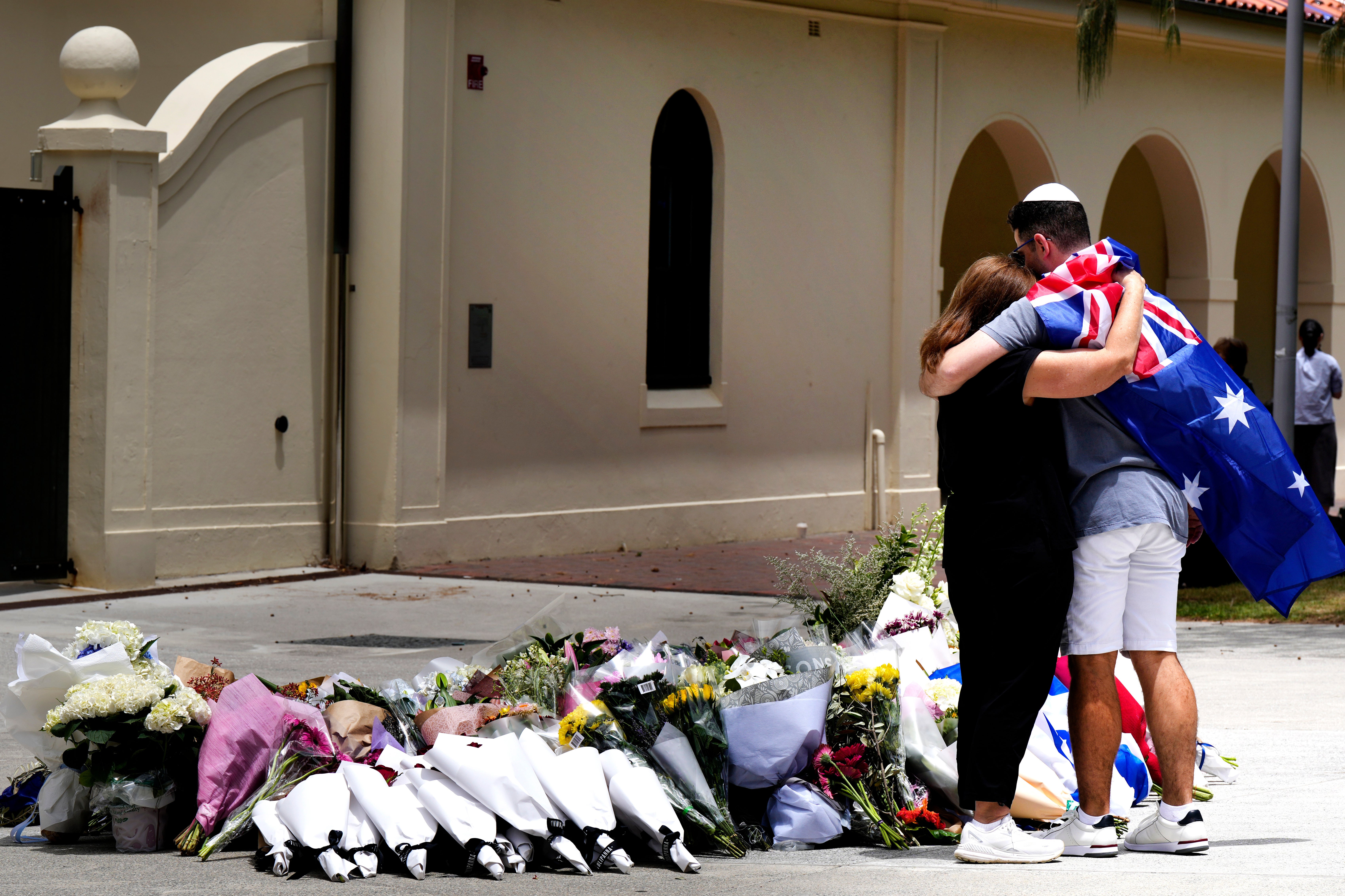 Un homme et une femme s’étreignaient devant le pavillon de Bondi, le 15 décembre 2025, près de nombreux bouquets de fleurs déposés en hommage aux victimes de l’attentat perpétré la veille contre une la foule de personnes qui célébraient la fête juive de Hanouka sur la plage de Bondi, à l’est de Sydney, en Australie.