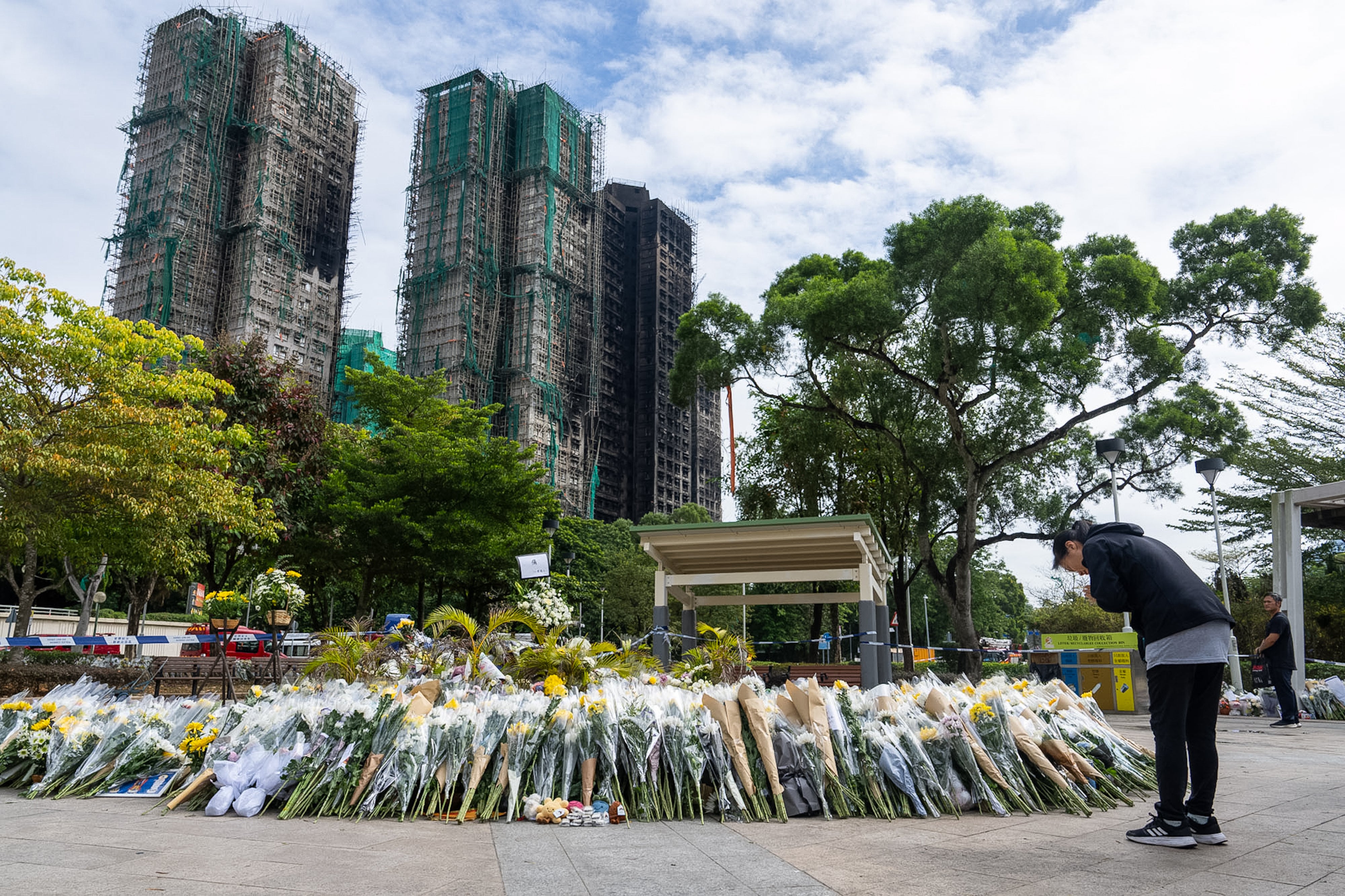 Une habitante de Hong Kong s’inclinait devant un espace transformé en mémorial à proximité des tours calcinées du Wang Fuk Court, un complexe résidentiel du quartier de Tai Po, le 1er décembre 2025 ; le 26 novembre, un incendie majeur y a tué au moins 151 personnes 