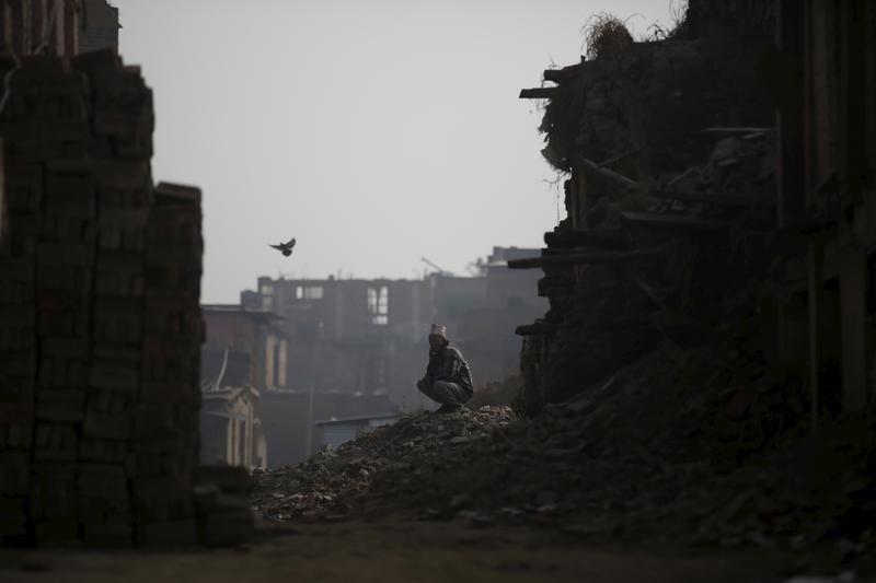 A man sits on top of the debris of houses damaged during the earthquake last year in Bhaktapur, Nepal, January 29, 2016.