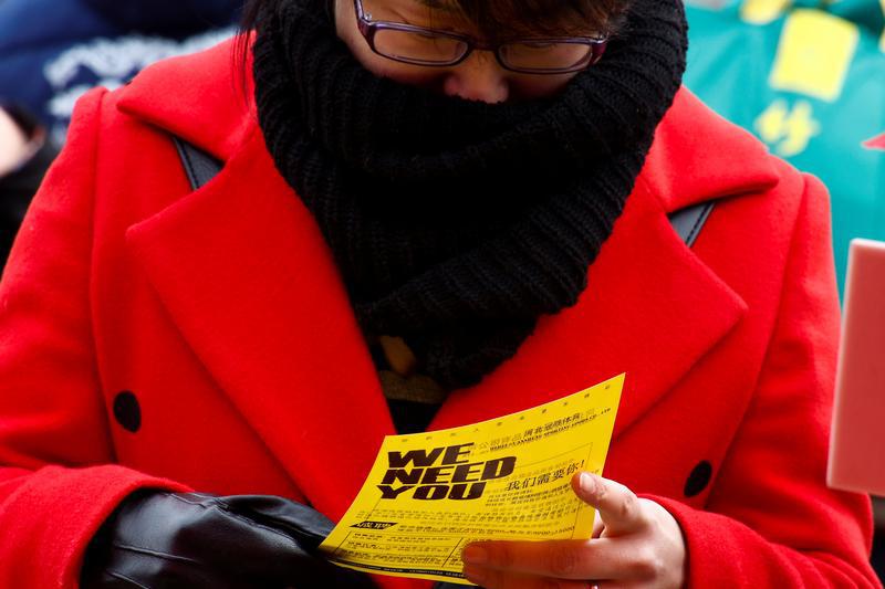 A woman reads a company flyer at an open air job fair for college graduates and the general public in the centre of Shijiazhuang, Hebei province, China, February 6, 2017.