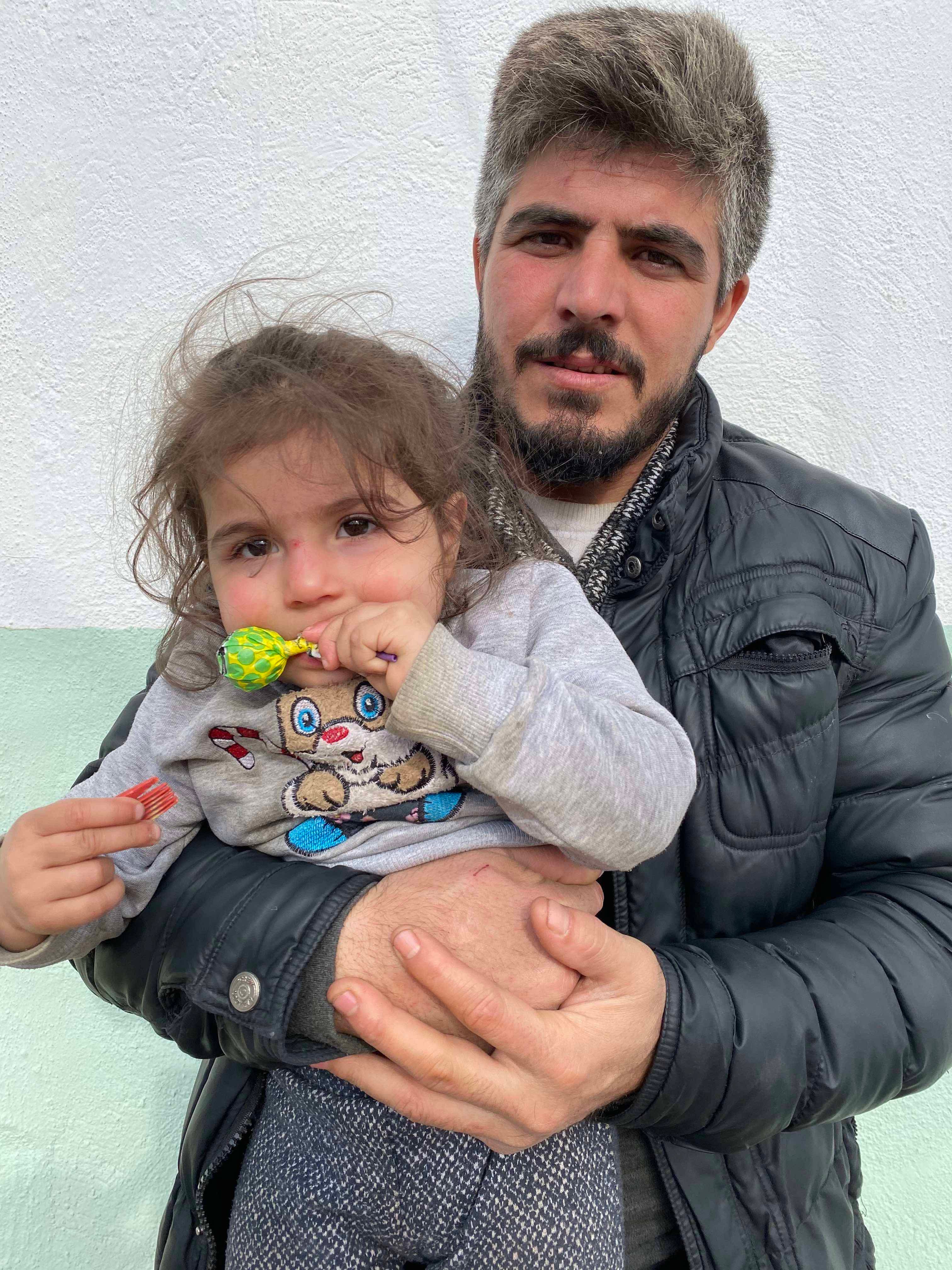 A Syrian man holds his 2-year-old daughter in the Turkish border village of Alibey on March 9, 2020, a day after he says Greek security forces detained and beat them both when he tried to stop them from sexually assaulting and stripping his wife.