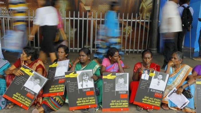 In this April 6, 2015, file photo, Sri Lankan ethnic Tamil women sit holding placards with portraits of their missing relatives as they protest out side a railway station in Colombo, Sri Lanka.