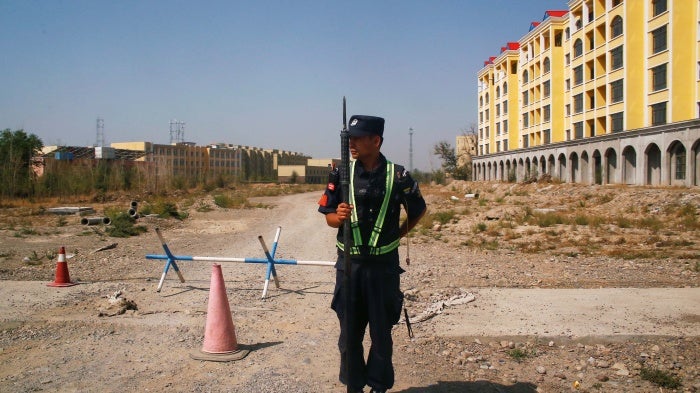 An armed police officer stands on a road leading towards a large yellow building
