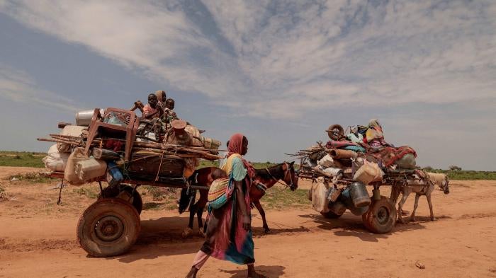 A Sudanese woman, who fled the conflict in Murnei in Sudan's Darfur region, walks beside carts carrying her family belongings upon crossing the border between Sudan and Chad in Adre, Chad, August 2, 2023.