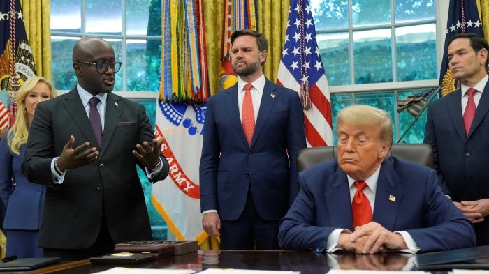 President Trump sitting in the Oval Office surrounded by aides 