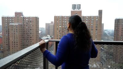 Woman standing on balcony looking at public housing buildings.