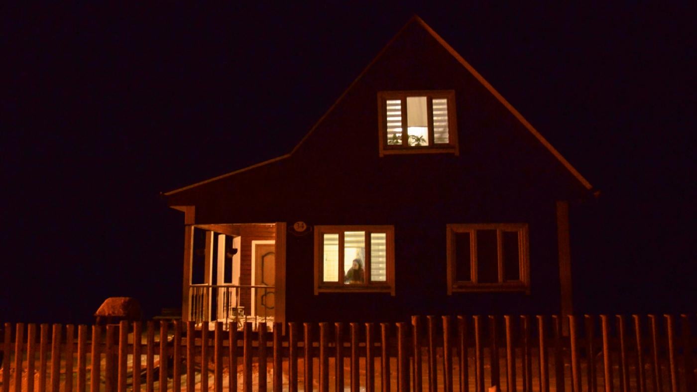 Yulia Alsheuskaya looking through the window of her house outside of Minsk, which she shares with her husband Siarhei who is currently in detention, January 2021.