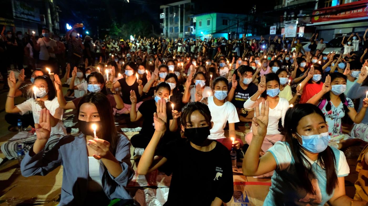 Protesters flash the three-fingered salute and hold candles during a rally at night in Yangon, Myanmar, March 14, 2021.
