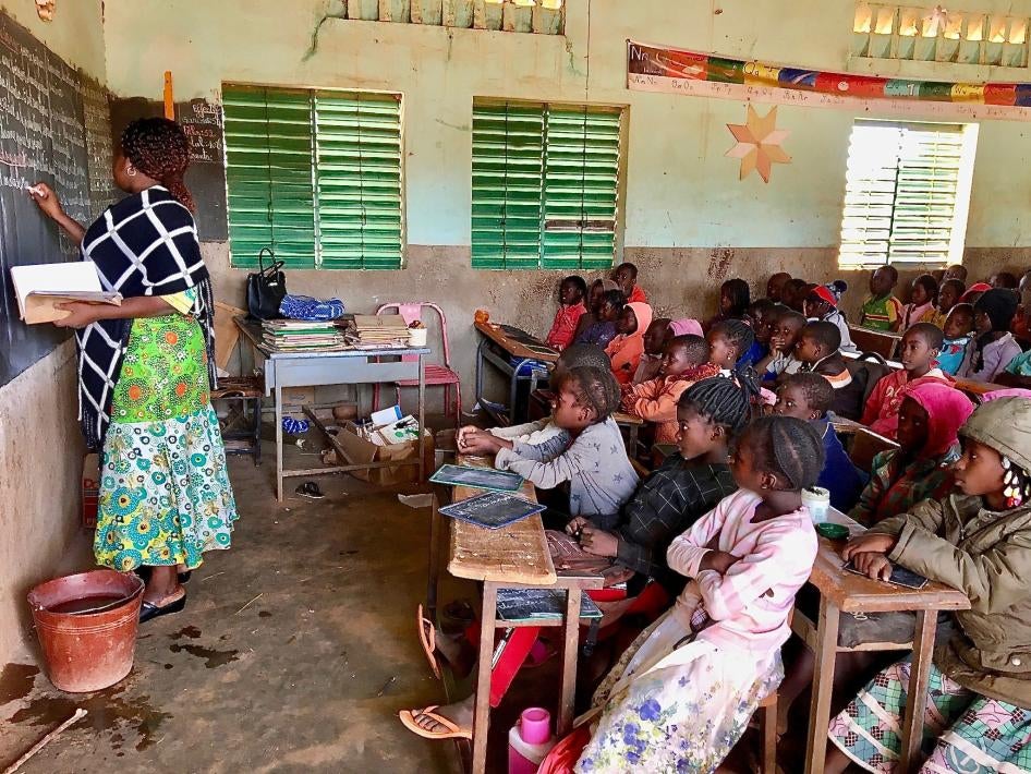 Young students watch a teacher write on a chalkboard