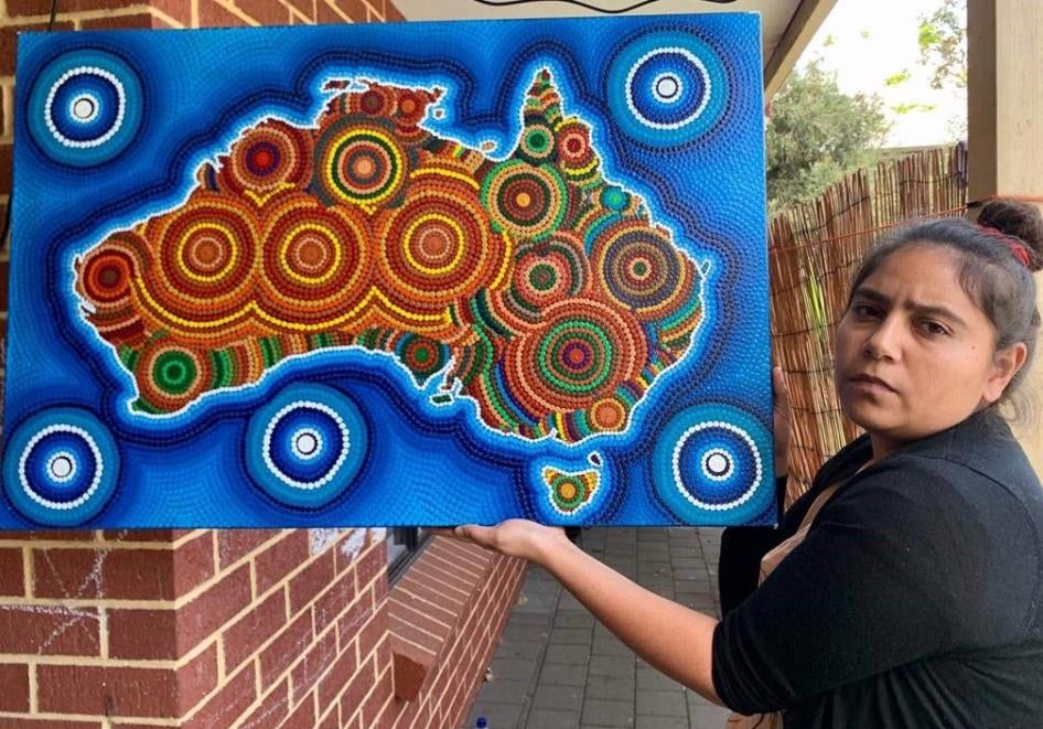 A woman holds up a colorful painting that depicts the Australian continent