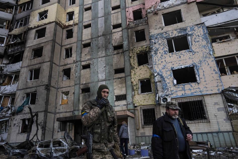 A soldier smokes a cigarette while walking next to a destroyed building