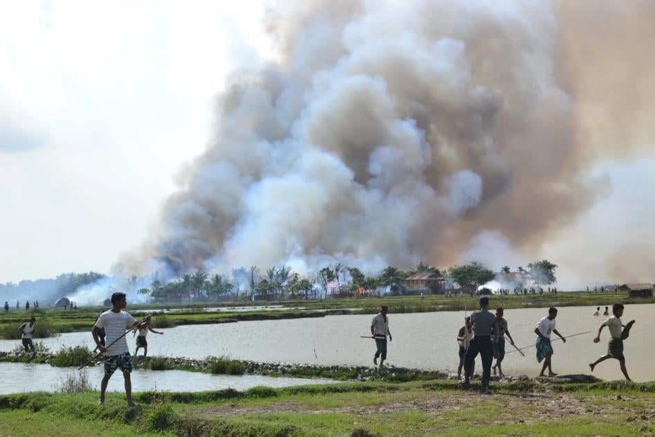 Ethnic Rakhine with weapons walk away from a village in flames while a soldier stands by, June 2012.