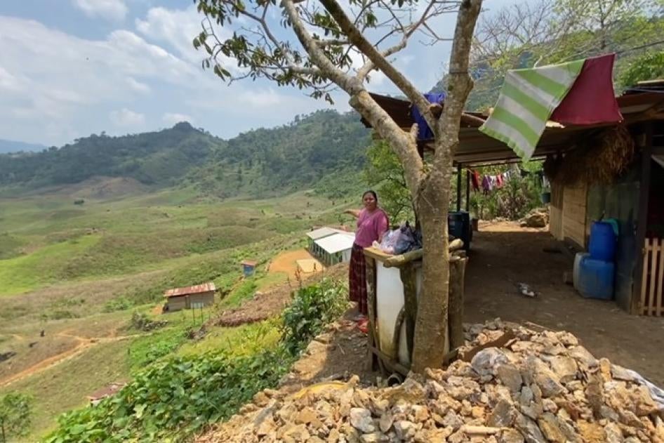 A woman points to white-roofed school in a valley below her home