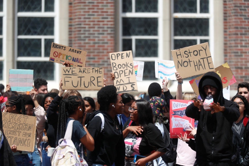 A group of high school students hold signs in front of a school building