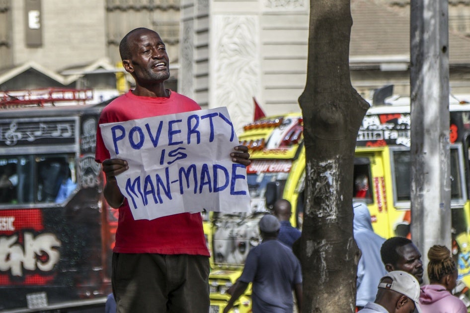 A man holds a poster that reads "poverty is man-made"