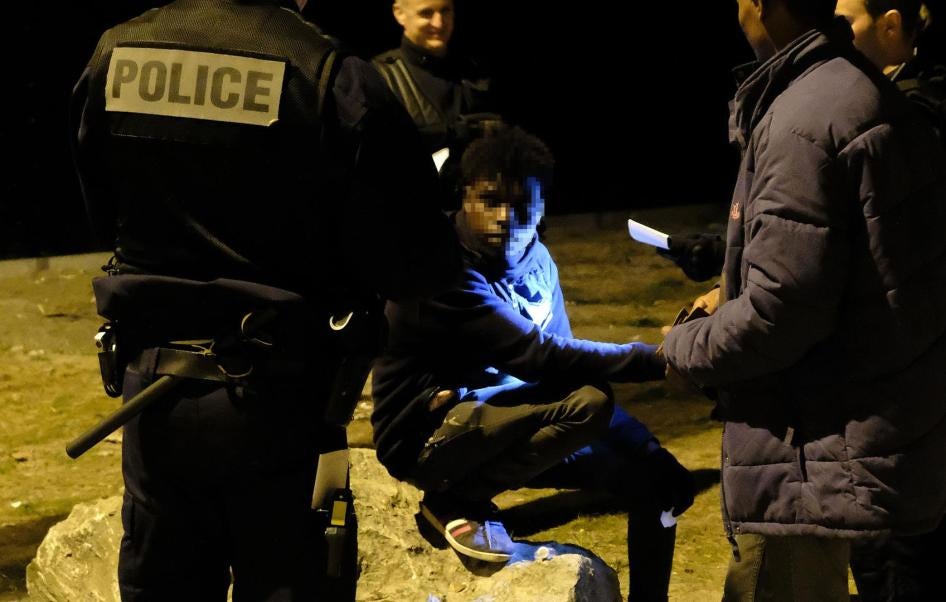 Police check identity documents after halting a distribution of food, water, and clothing in an industrial area of Calais shortly after midnight on June 30, 2017.