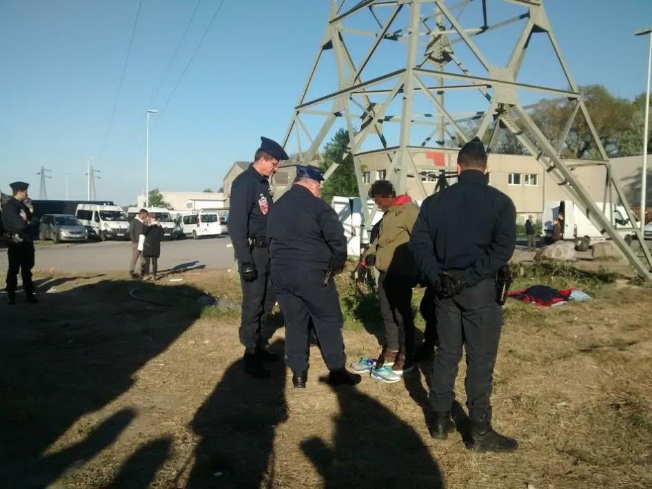 After police halted an evening distribution of food and clothing, three officers stop and question a boy who had paused to change his shoes before returning to the wooded area where he and other migrants spend the night, May 2017. © 2017 Help Refugees