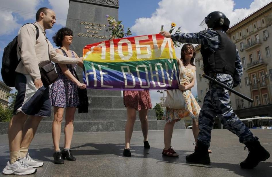 Participants in a LGBT community rally in central Moscow, Russia hold a rainbow flag that reads, "Love. Don't make war", as a policeman stops them.