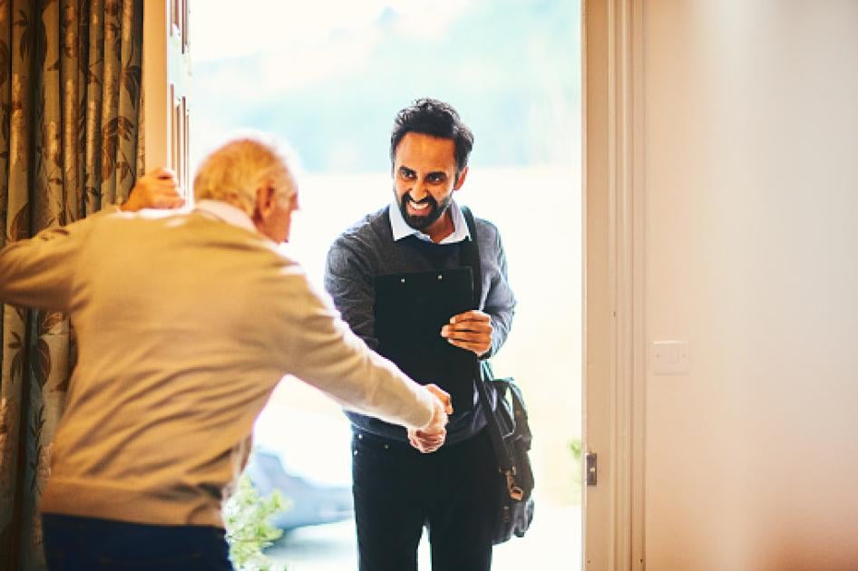 Young male community healthcare worker being welcomed by a senior man at his home. 
