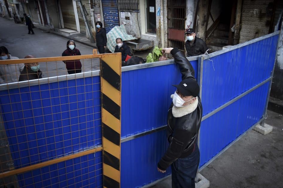 A man wearing a protective face mask passes groceries through the barricades blocked a residential area in Wuhan in central China's Hubei province, February 23, 2020. 