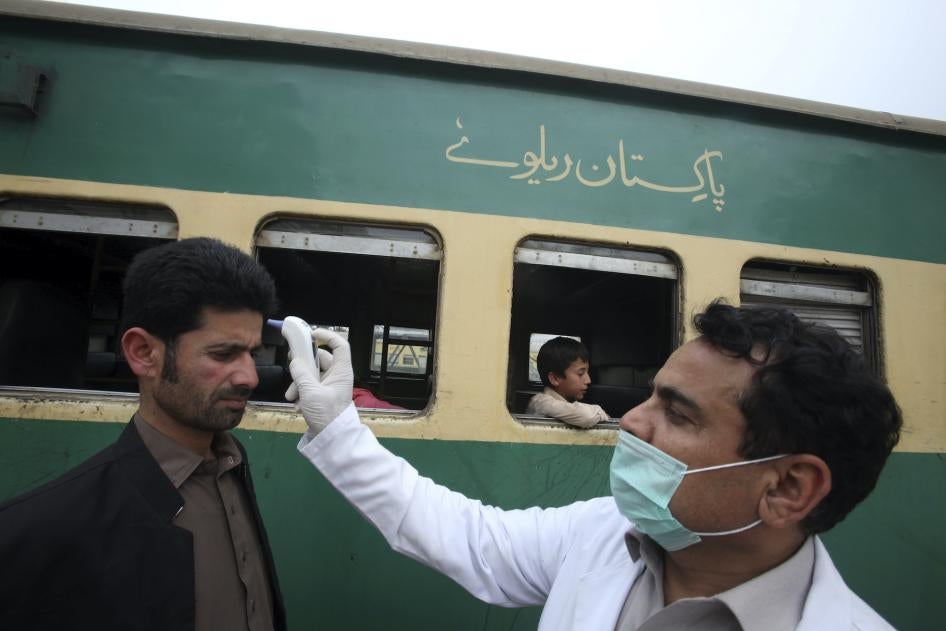 A volunteer checks the temperature of passengers arriving at a railway station in Peshawar, Pakistan, March 17, 2020.