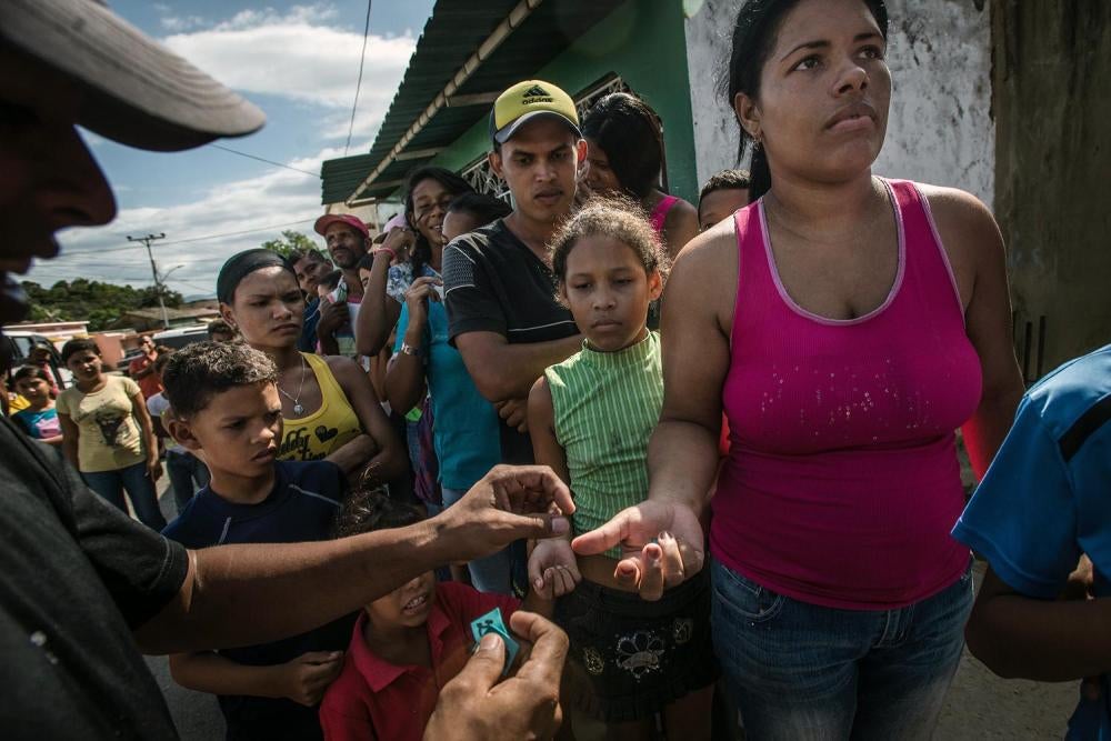 A bakery worker passes out numbers to scores of shoppers, many of whom had been waiting in line for five hours, entitling them to buy a half-kilo ration of bread in Cumaná, June 16, 2016.