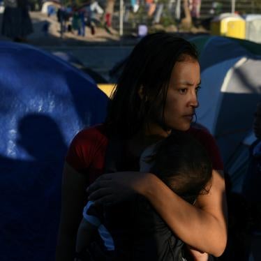 A woman holds a child in front of a group of tents
