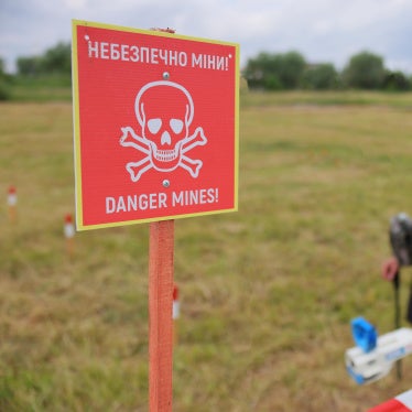 Sign saying "danger mine" in Ukrainian and English with deminers in the background.