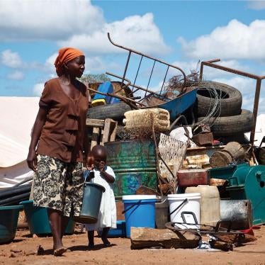  A woman stands in front of a pile of her household property at Chingwizi transit camp, which the government forcibly shut down in August 2014. Hundreds of families lost their property left in the open during their relocation to the camp. March 2014.