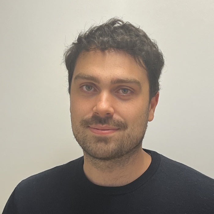 Man in black sweater with dark hair and light colored eyes poses for professional headshot.