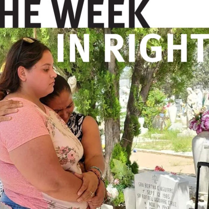 Two people embrace in front of memorial. 
