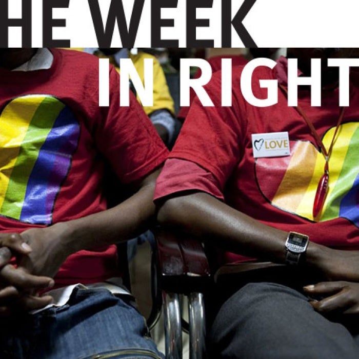 Two individuals in pride shirts hold hands.